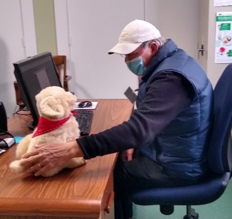 Older man sitting at a computer desk petting a soft robotic dog.