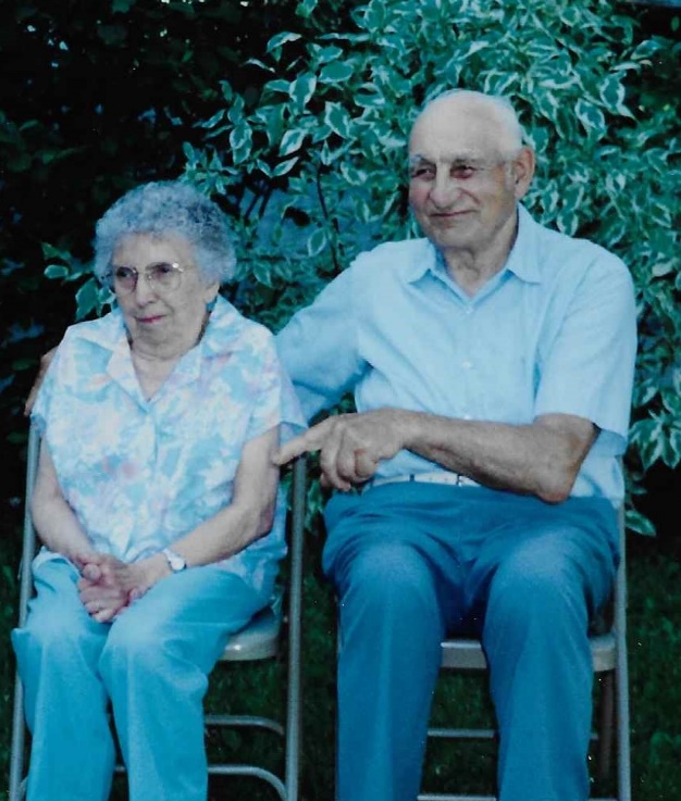 Older white man and woman smiling and seated in front of a garden